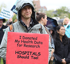 Protester holding sign: ''I donated my health data for research ... hospitals should too''